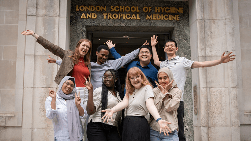 Group of students posing with arms open on the front steps of LSHTM in Keppel Street.